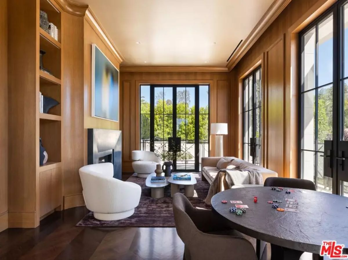 Wood-paneled room with poker table, lounge chairs, and multiple glass doors opening to exterior.
