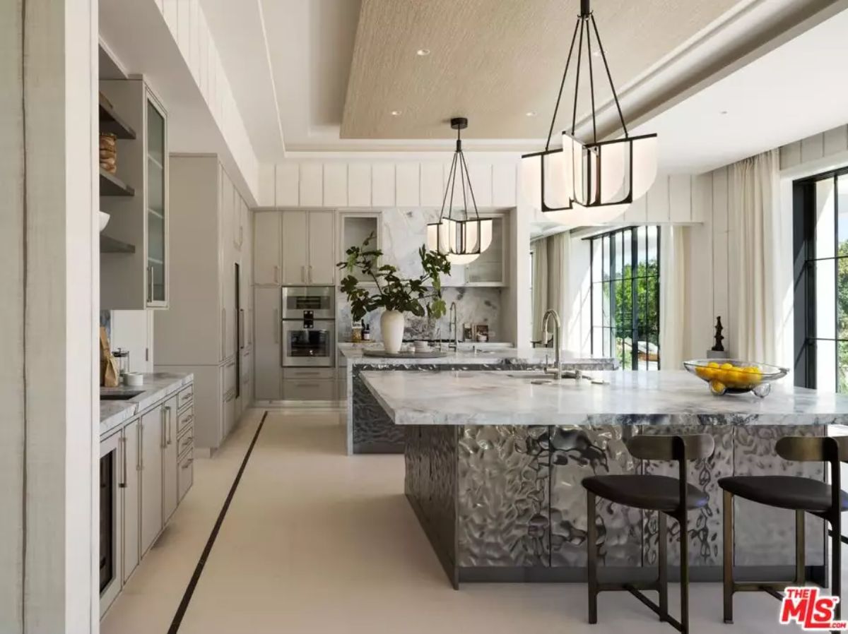 View of kitchen from entry showing twin marble islands, light fixtures, and floor-to-ceiling cabinetry.