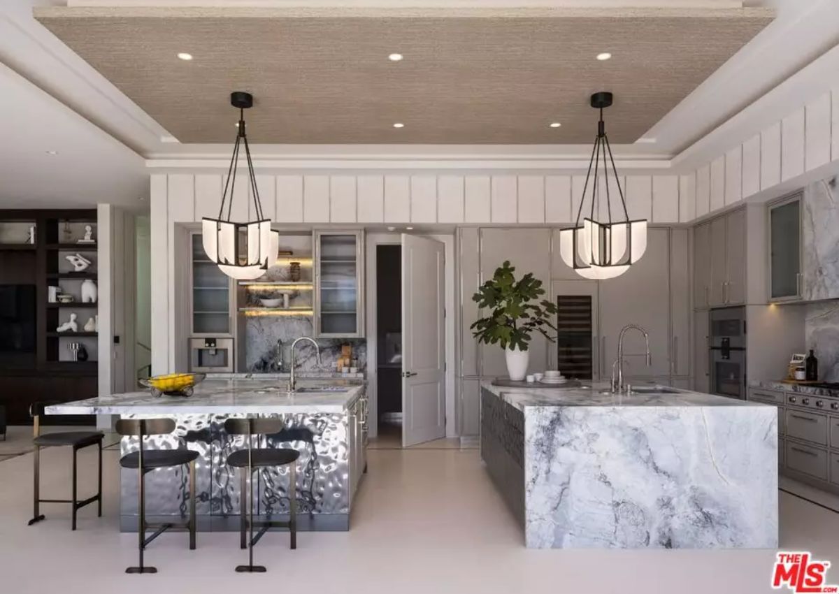 Kitchen with two marble islands, pendant lighting, built-in shelving, and integrated appliances.