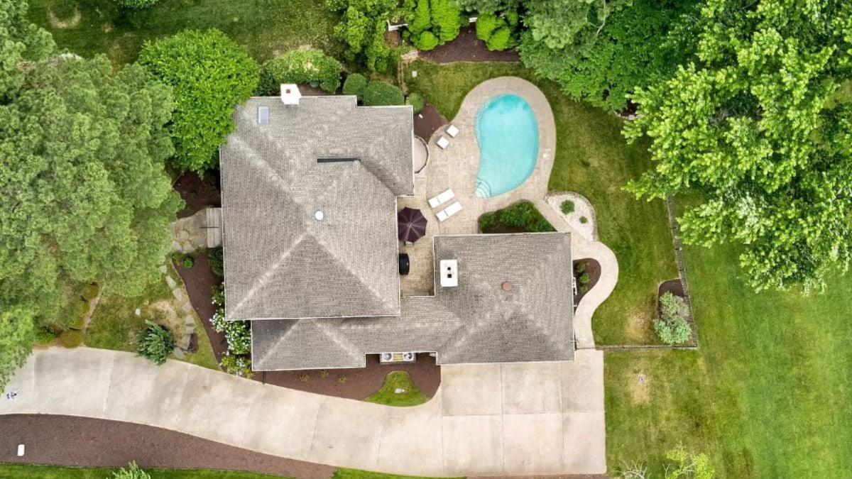 Aerial View of a Home with a Curved Driveway and Serene Poolside Setting