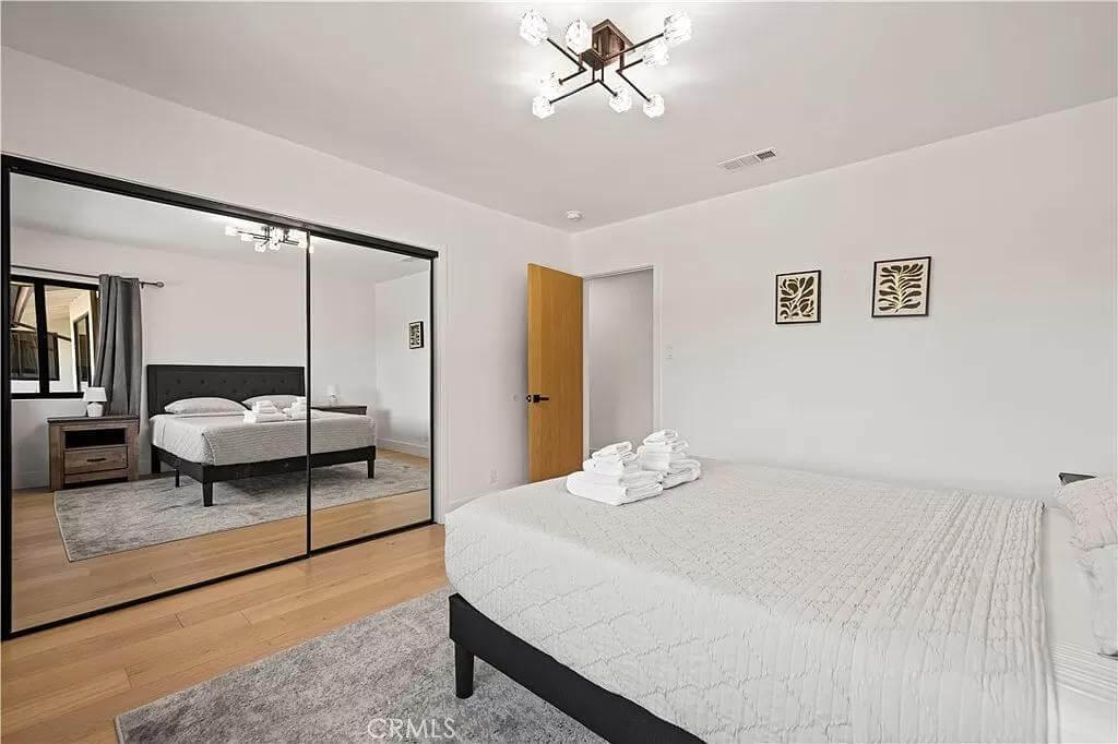 Minimalist Bedroom with Sleek Mirrored Closets and a Subtle Geometric Light Fixture