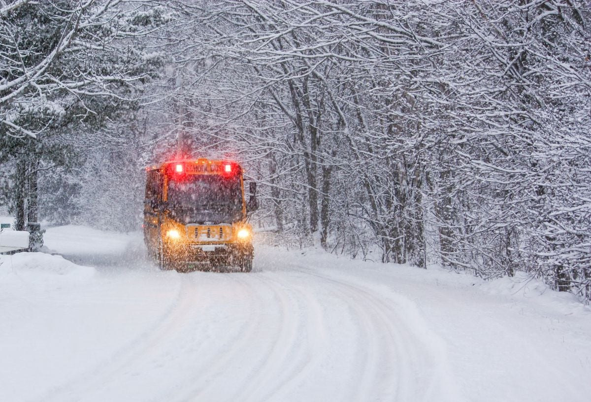 A school bus in a winter storm traveling on a deep snow covered rural road.