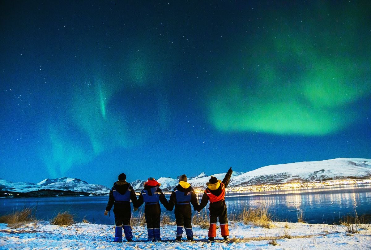 Group Tourists experiencing Northern Lights dancing over the night sky. 