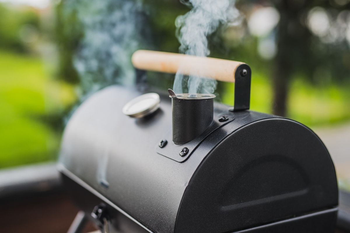 Smoke coming out of a smokestack of a small black smoker grill or barbecue.