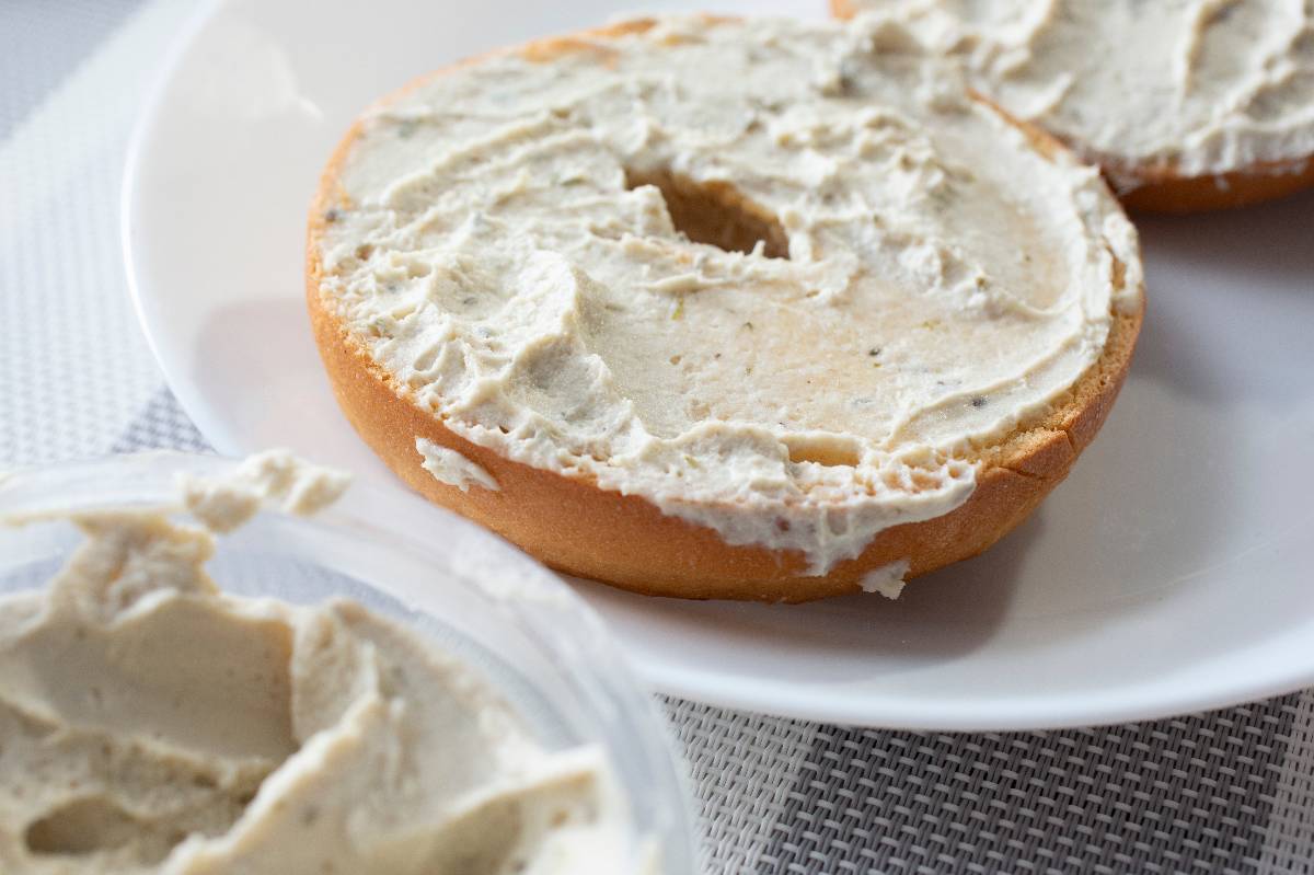 A closeup view of gluten-free bagel slices on a plate, smeared with dairy-free cream cheese.