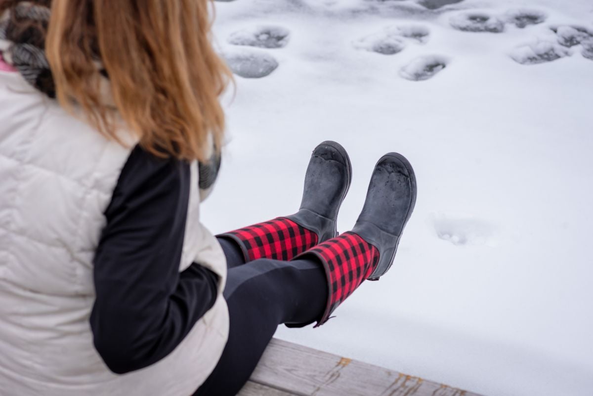 Woman sitting on wooden pier looking at her red plaid boots.