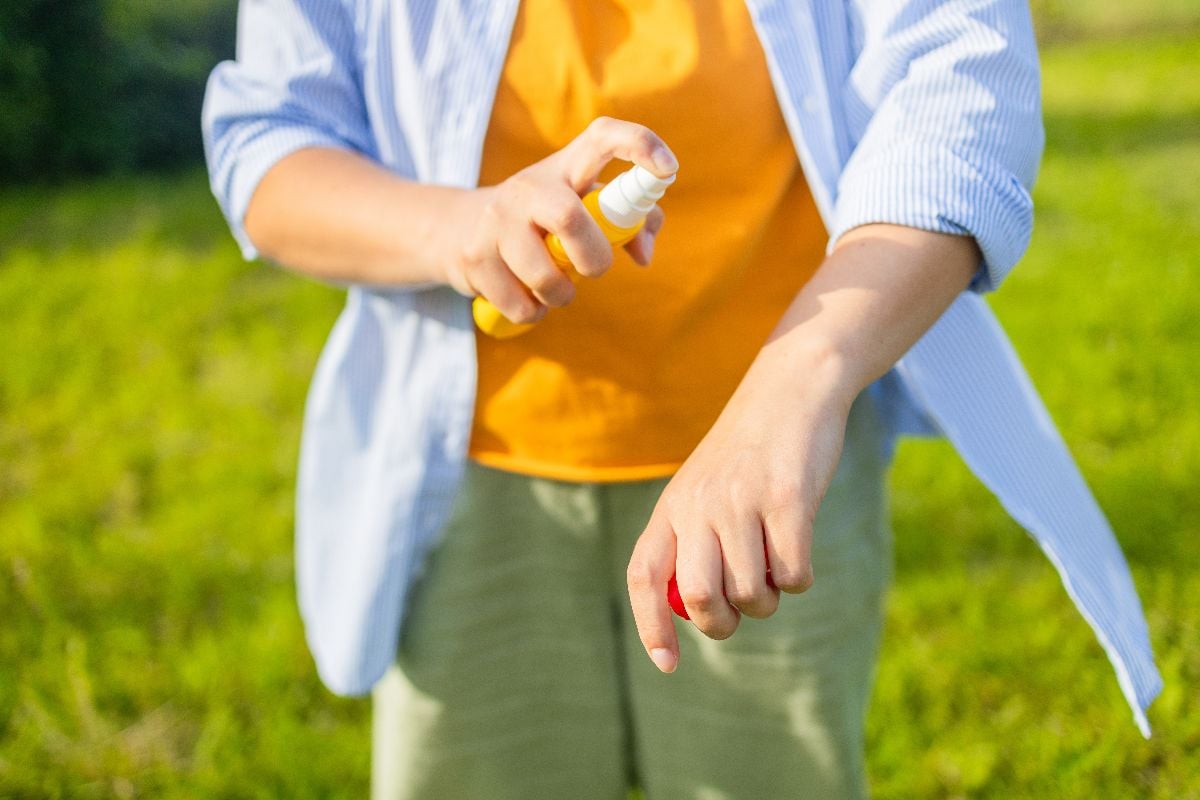 Woman applying bug repellent spray outdoors.