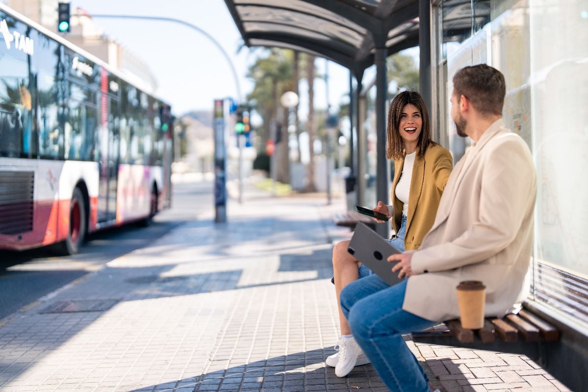 Two friends sitting at bus station, having a conversation.