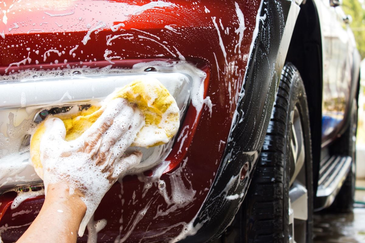 Man washing front fog light of a red car.