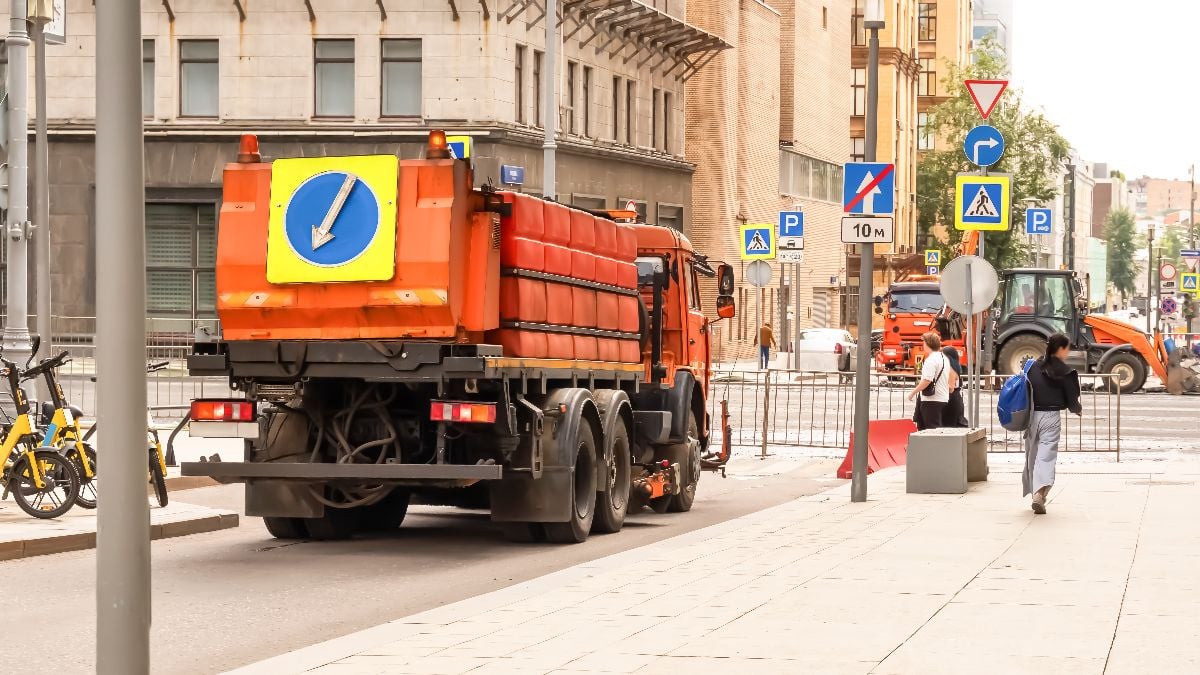 Street maintenance vehicle working on urban road with construction signs and equipment.