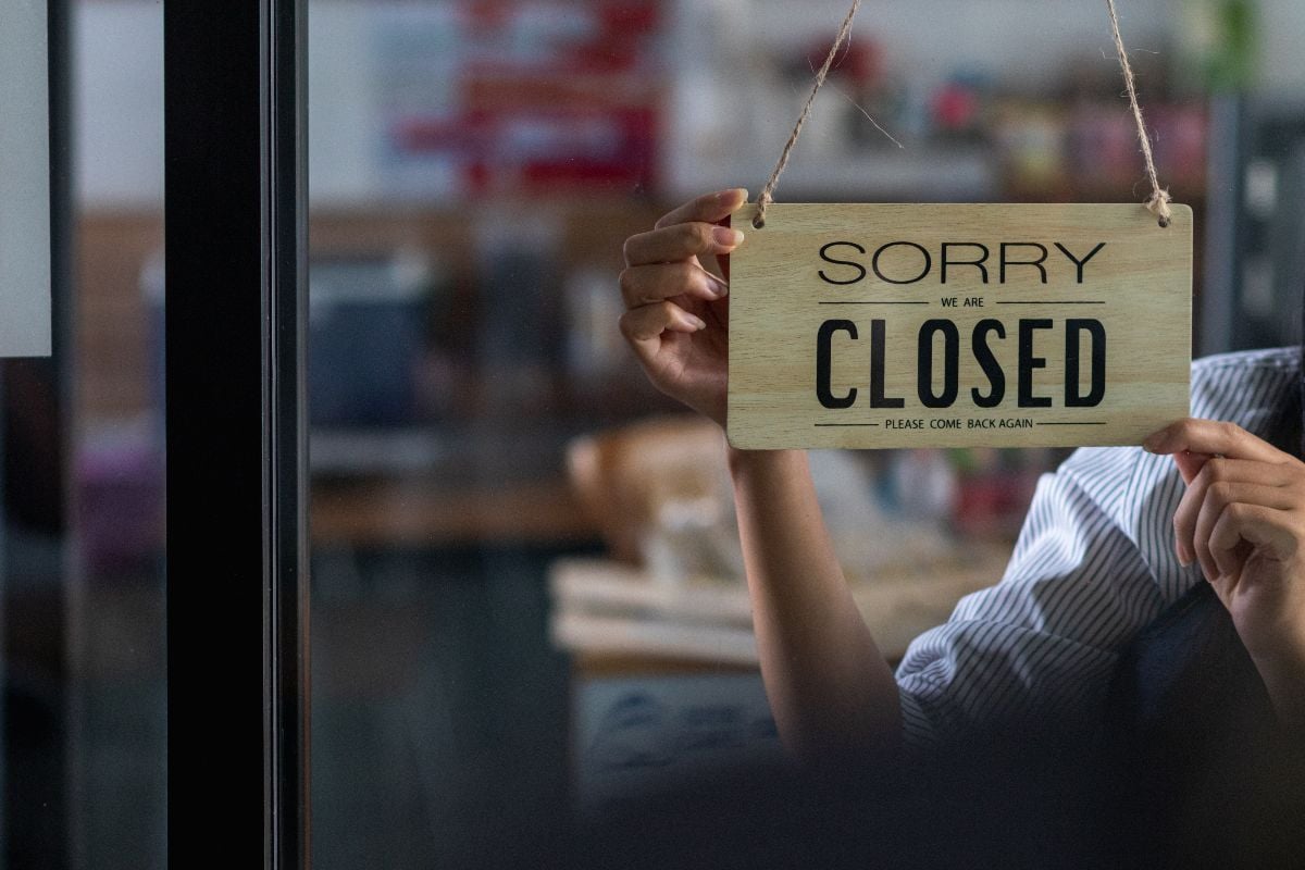 The shop owner puts a closing sign on the glass door of the shop.