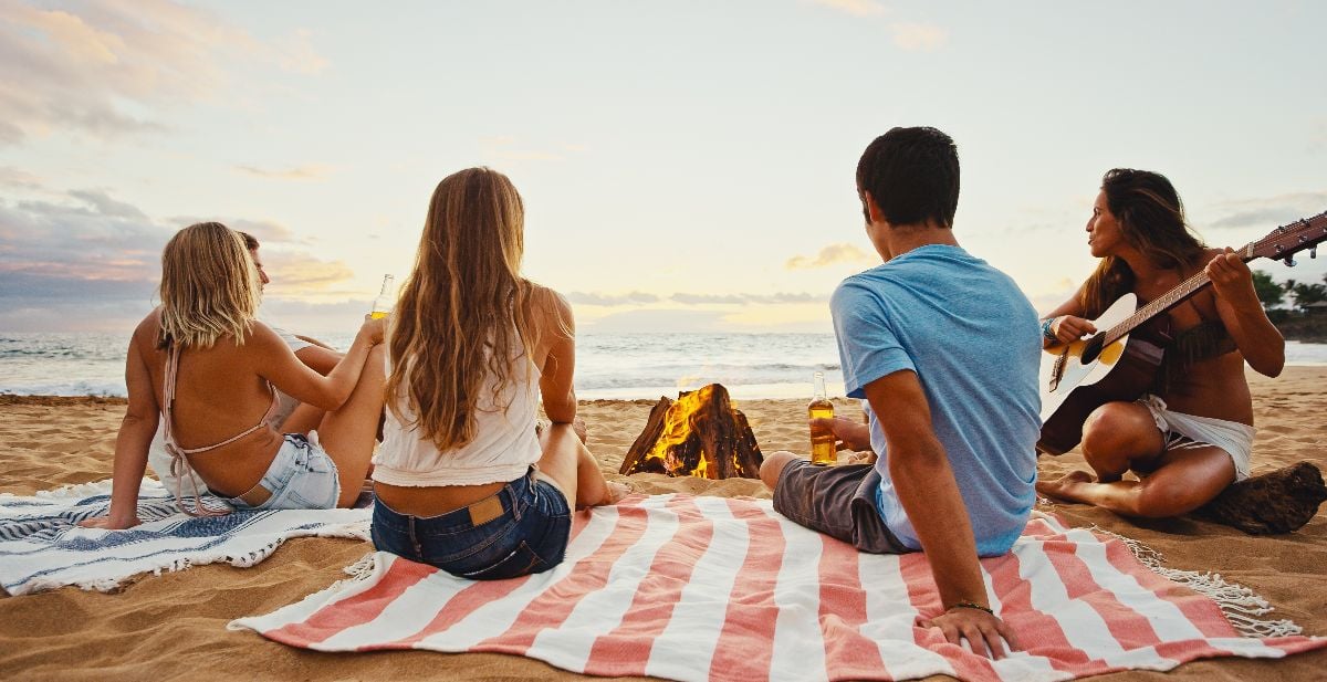 Group of friends relaxing around bonfire on the beach at sunset.