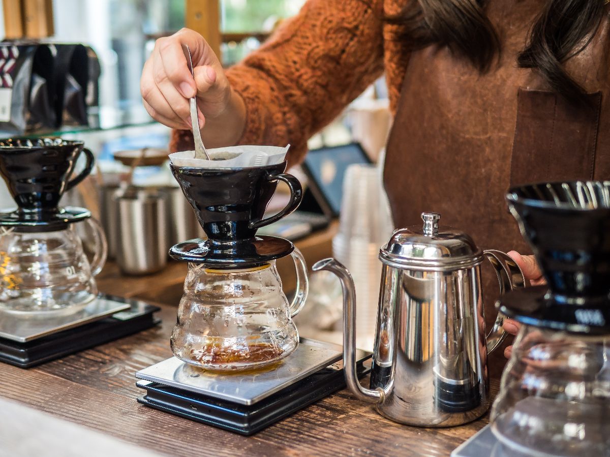 Barista pouring water over roasted, ground coffee beans.