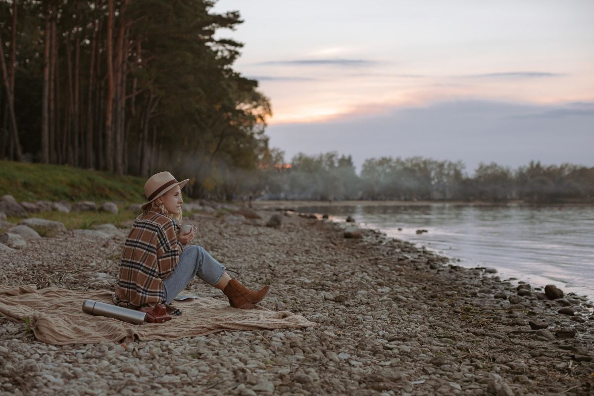Woman traveler in blue jeans, plaid shirt, and cowboy boots sitting on blanket looking out at view. 