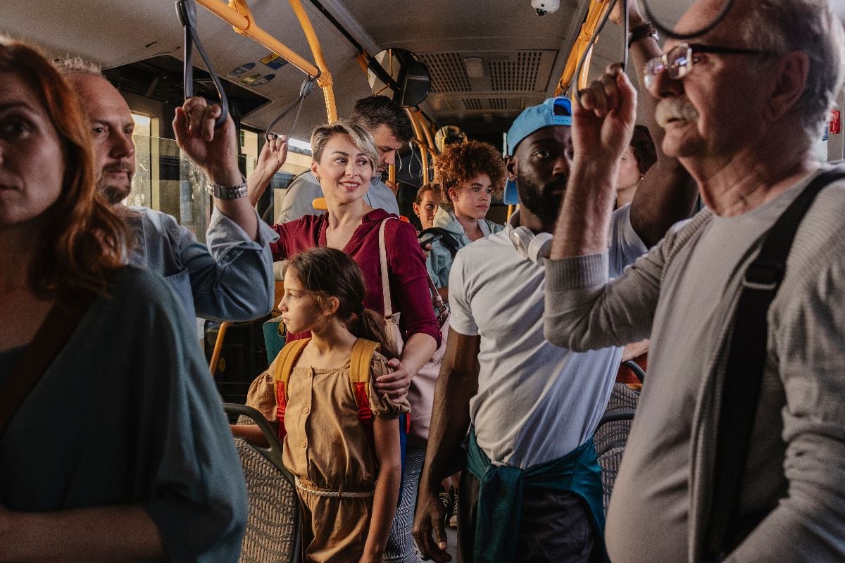A crowded bus with diverse commuters standing and holding onto handrails during a busy ride.