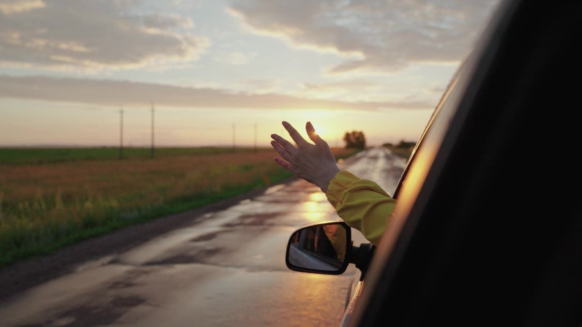 Girl in car window waves her hand and catches wind at sunset.