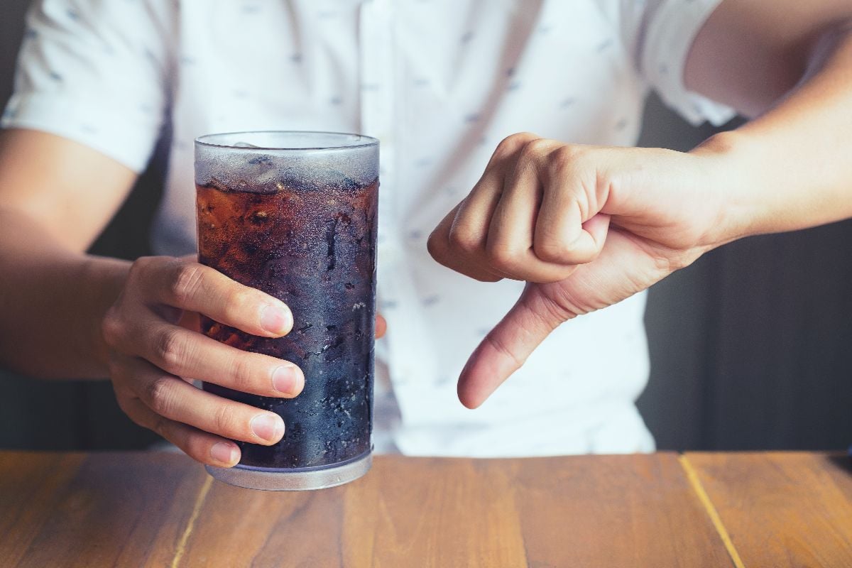 A man holding a soda with one hand gesturing thumbs down.