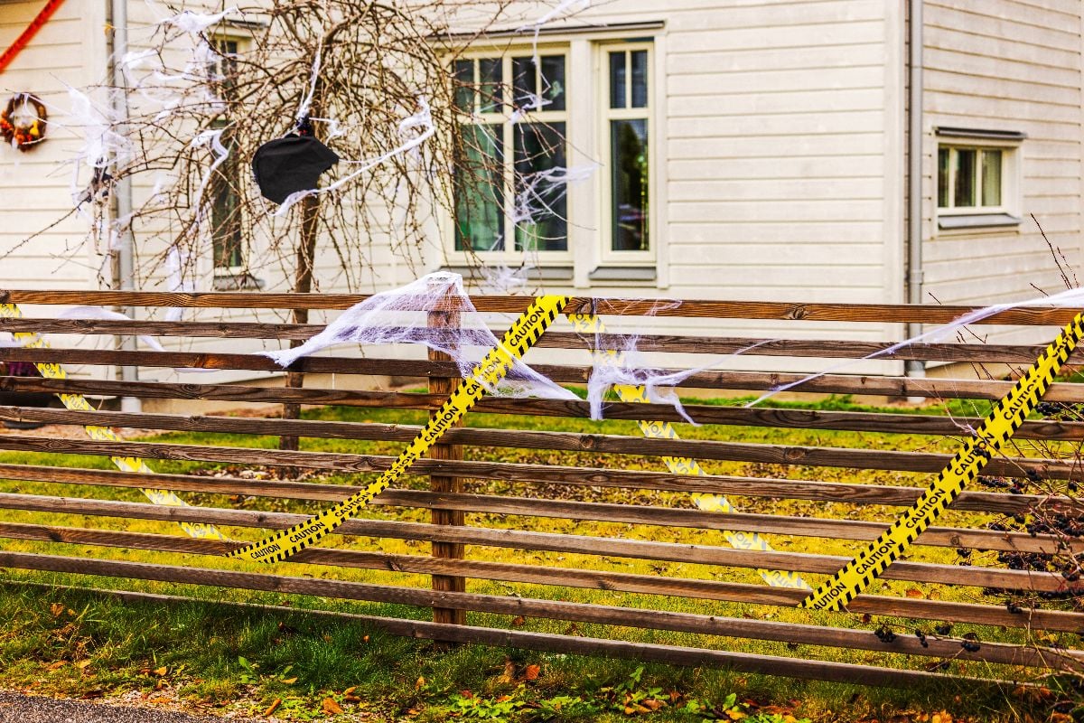 Halloween caution tape and spider webs on wooden fence 
