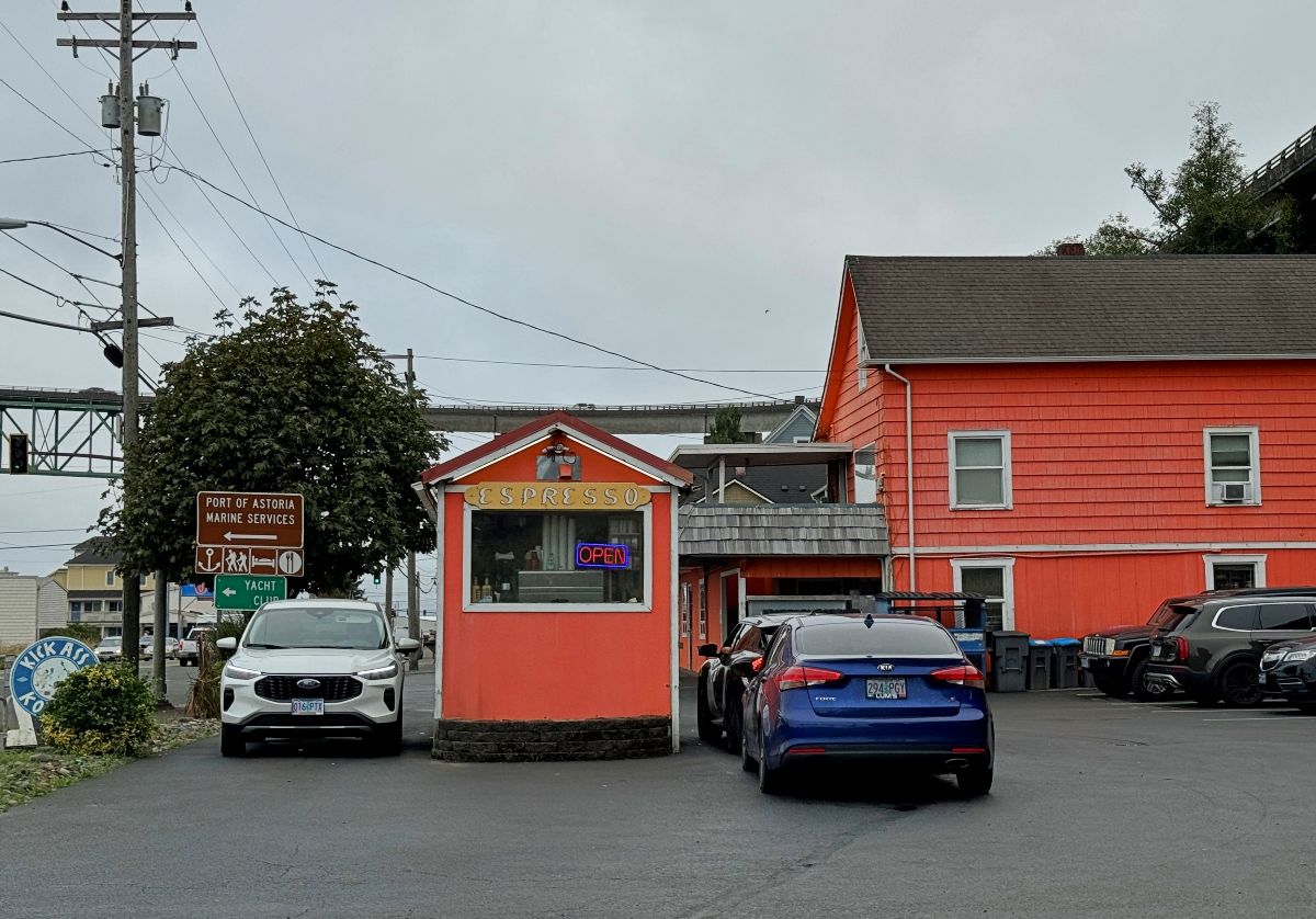 Small orange espresso stand with neon open sign and drive-thru traffic.