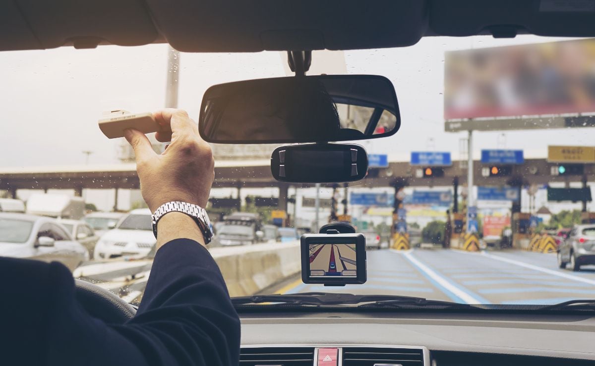 Man driving car and holding electronic toll collection system device.