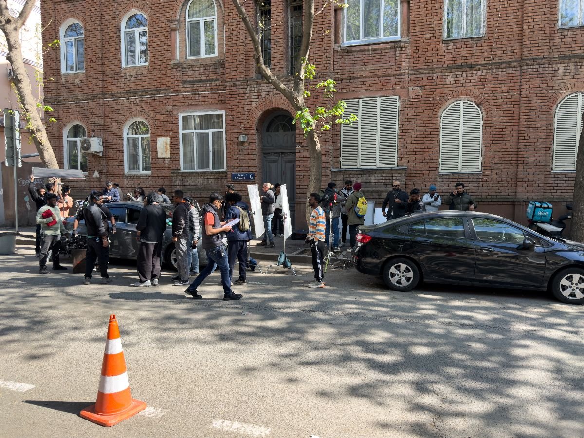 Film crew shoots scene on city street near brick building.