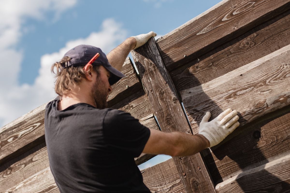Man builds sections of fence around his yard out of planks.