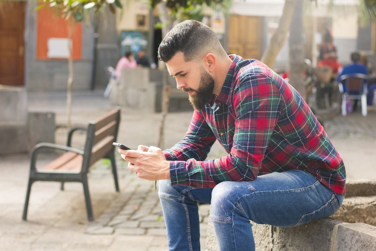 Man in red checkers flannel shirt holding smart phone outdoors.