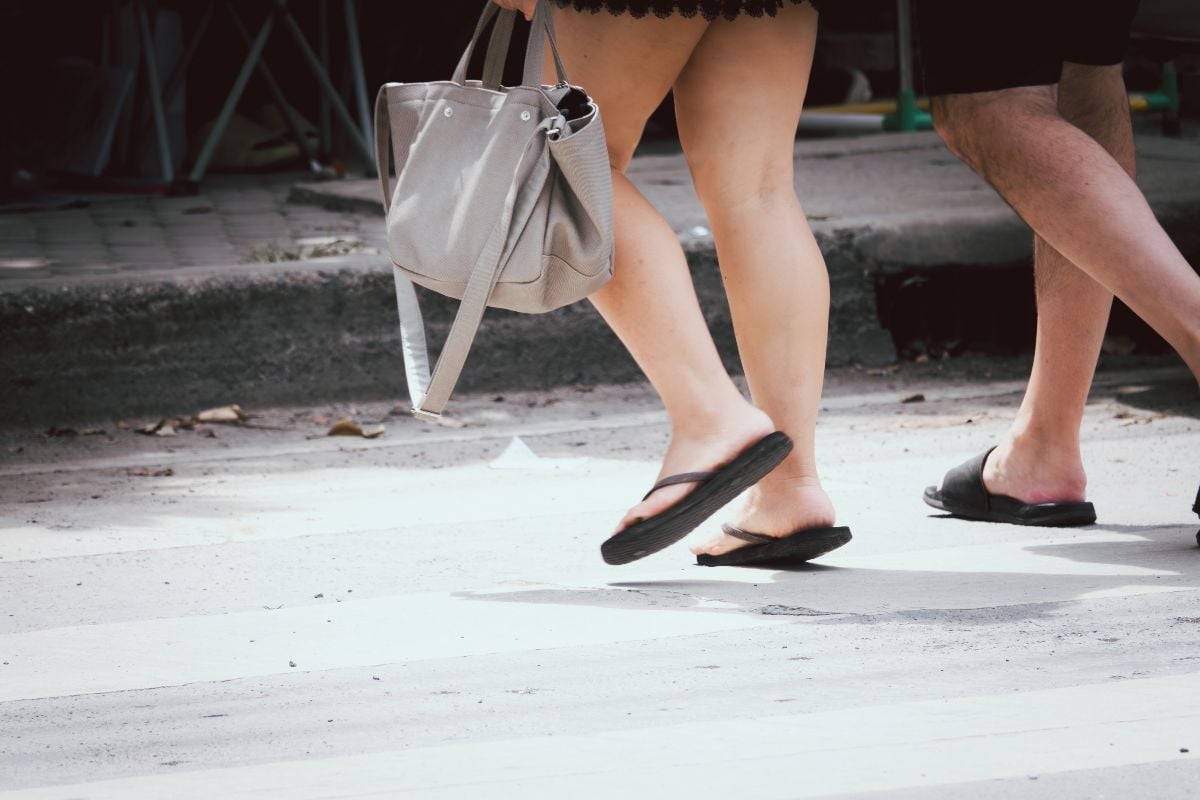 A woman walking down the street with her flip flops.