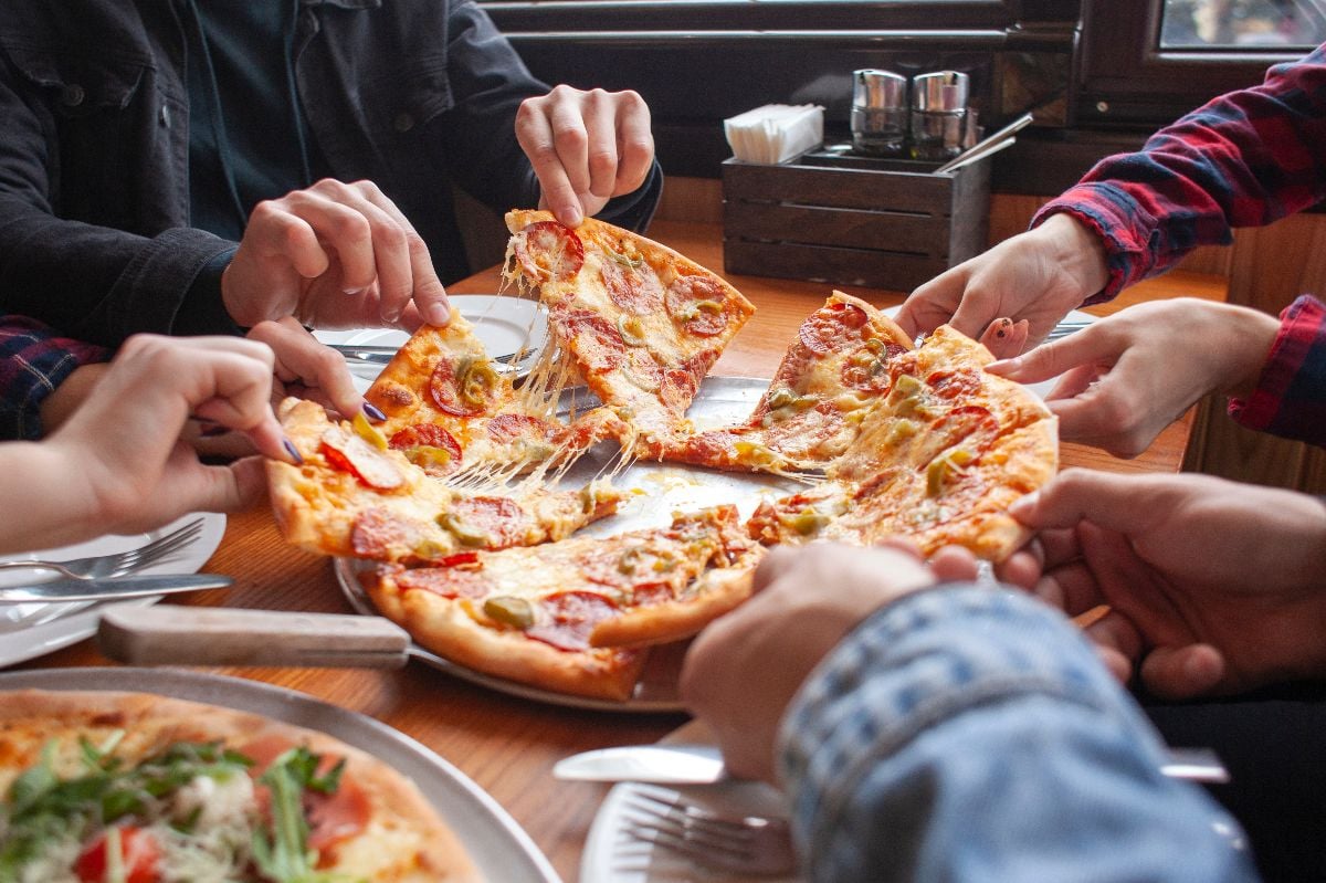 Group of friends taking slices of pizza in a restaurant.