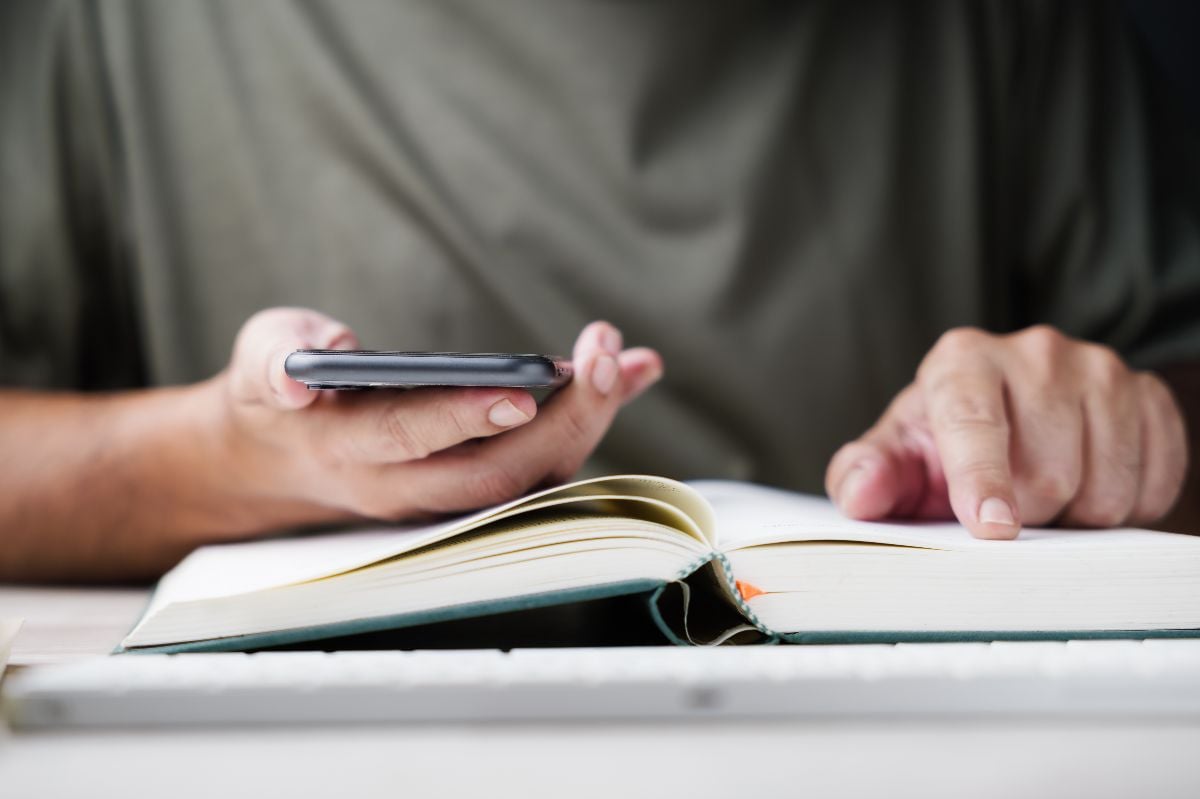 Man holding a phone and reading a book.