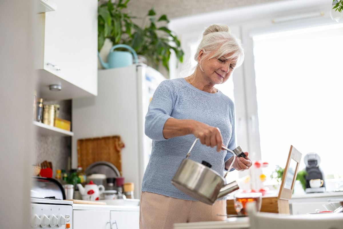Grandmother pouring water into teapot at home kitchen.