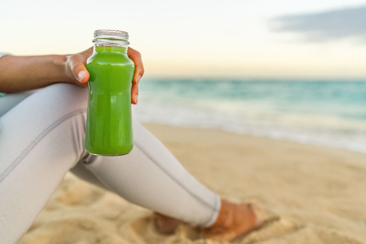 Woman holding a glass bottle of cold pressed vegetable in the beach.