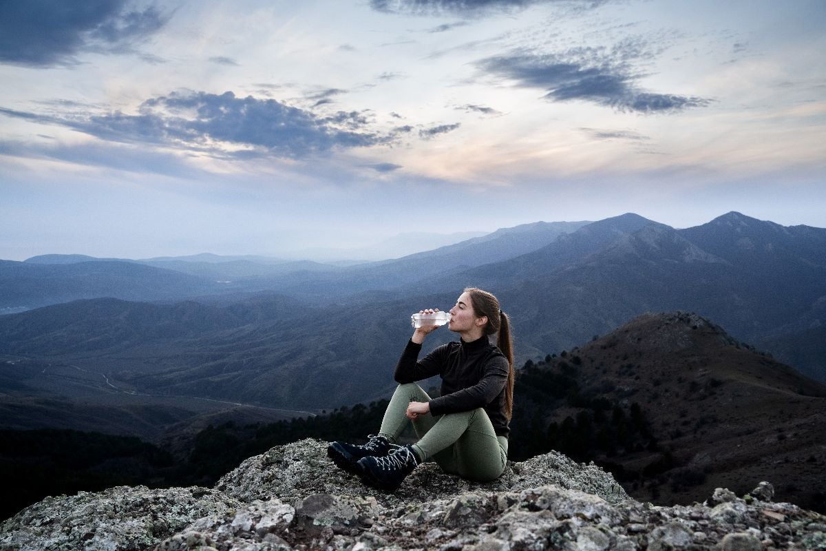 Woman drinking water while sitting on a cliff's edge during a hike.