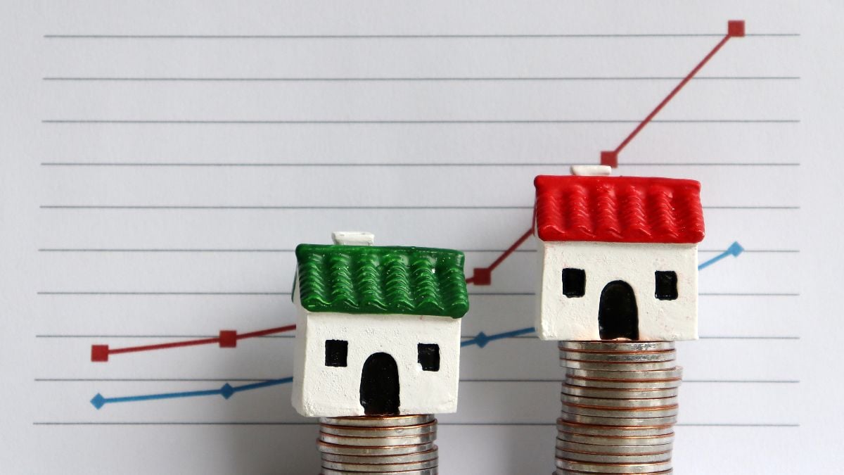 Two miniature houses on piles of coins in front of a graph.