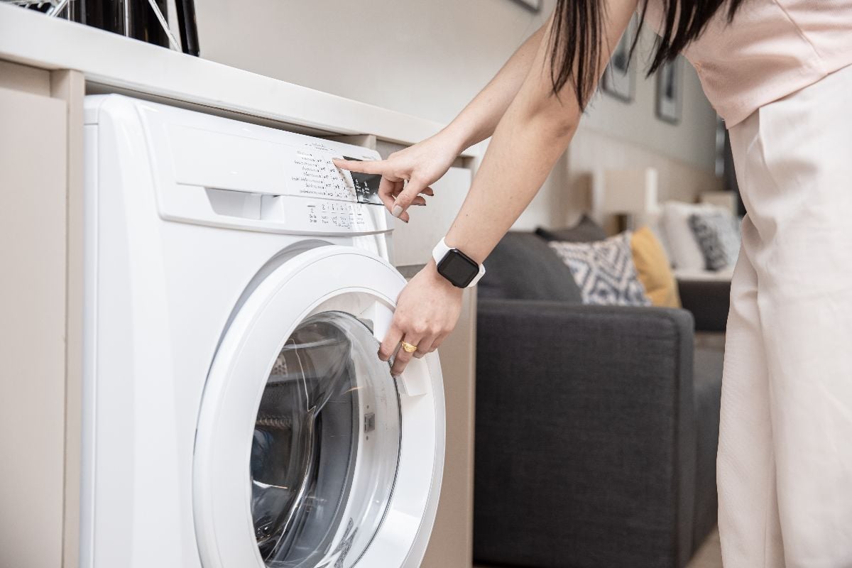 Women using front load washing machine in apartment.