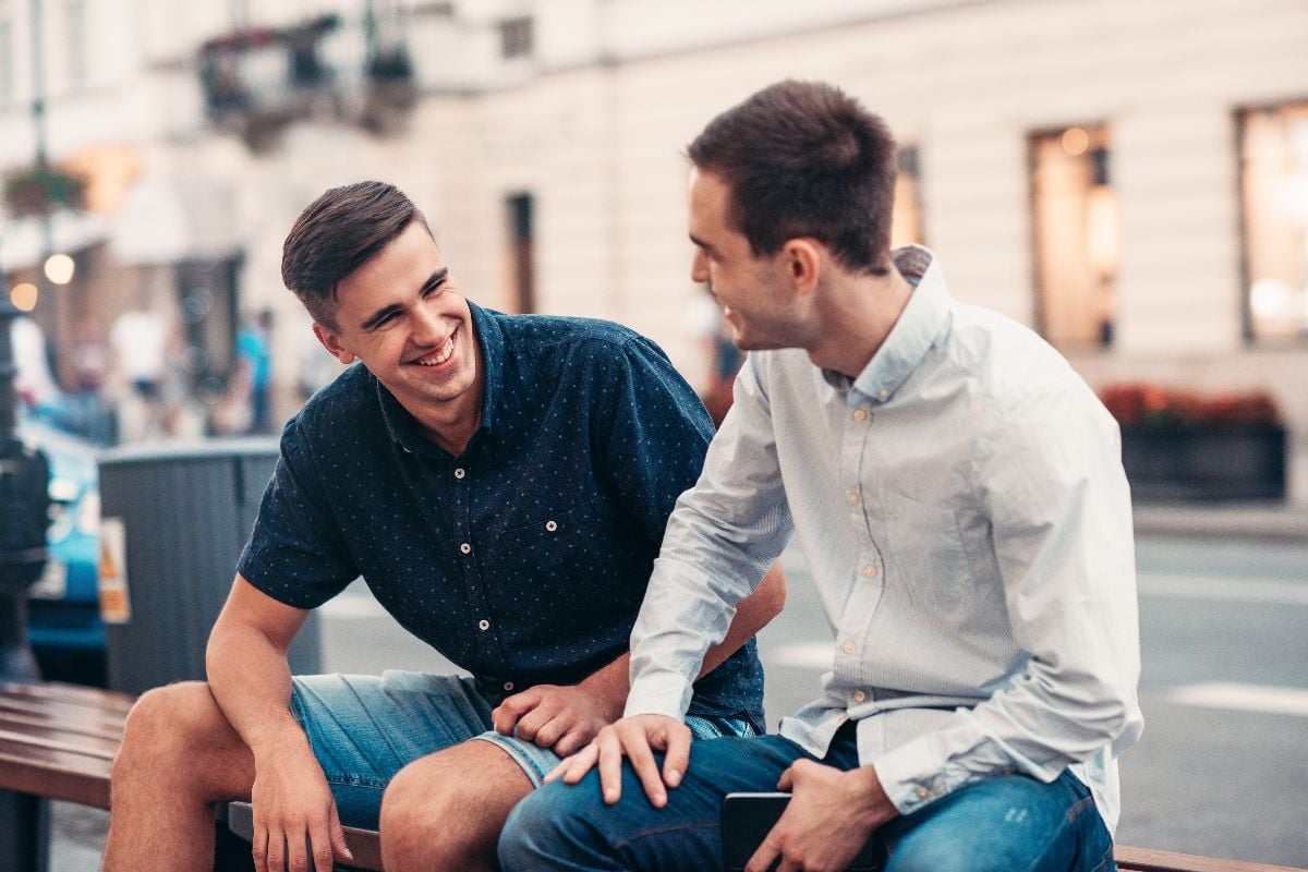 Friends talking together on a bench outdoors.