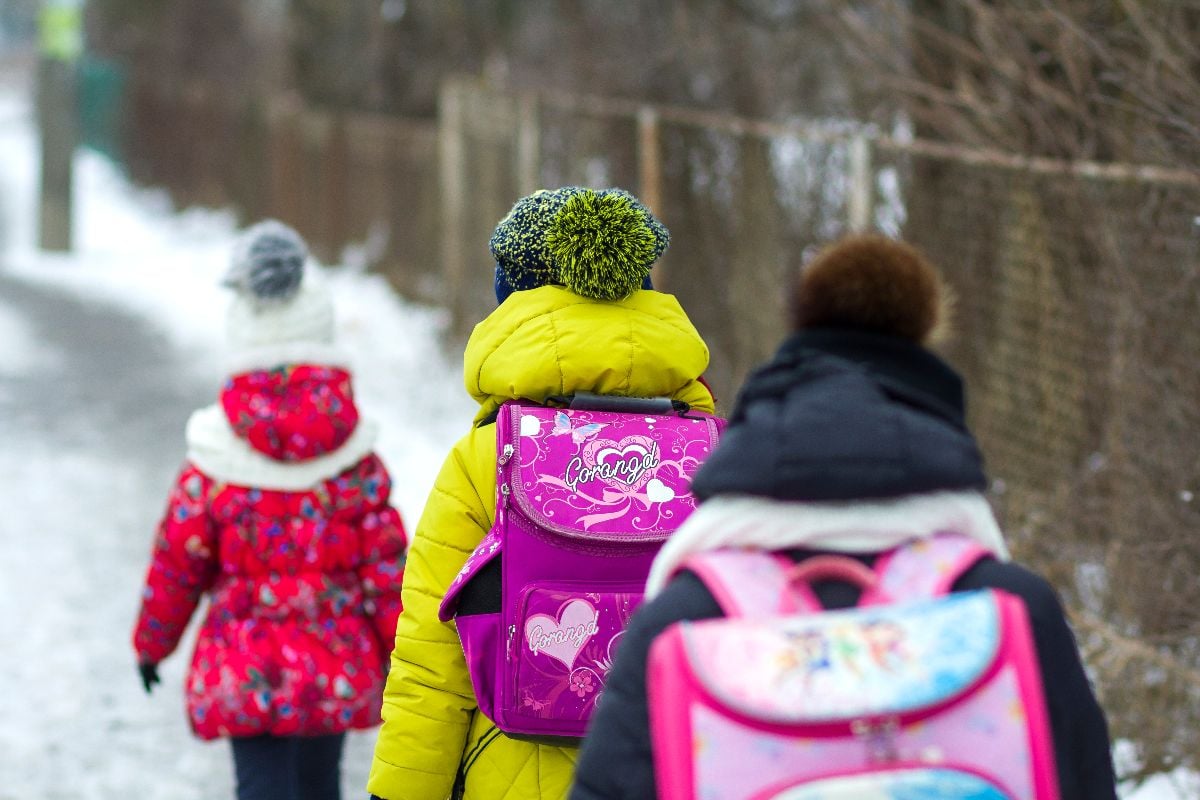 Group of elementary school children with backpacks walking outdoors in winter.