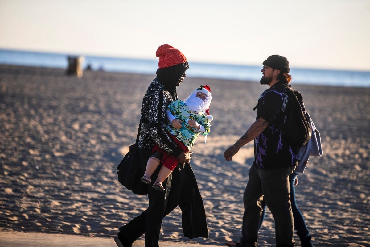 A parent walks along the beach carrying a miniature Santa.