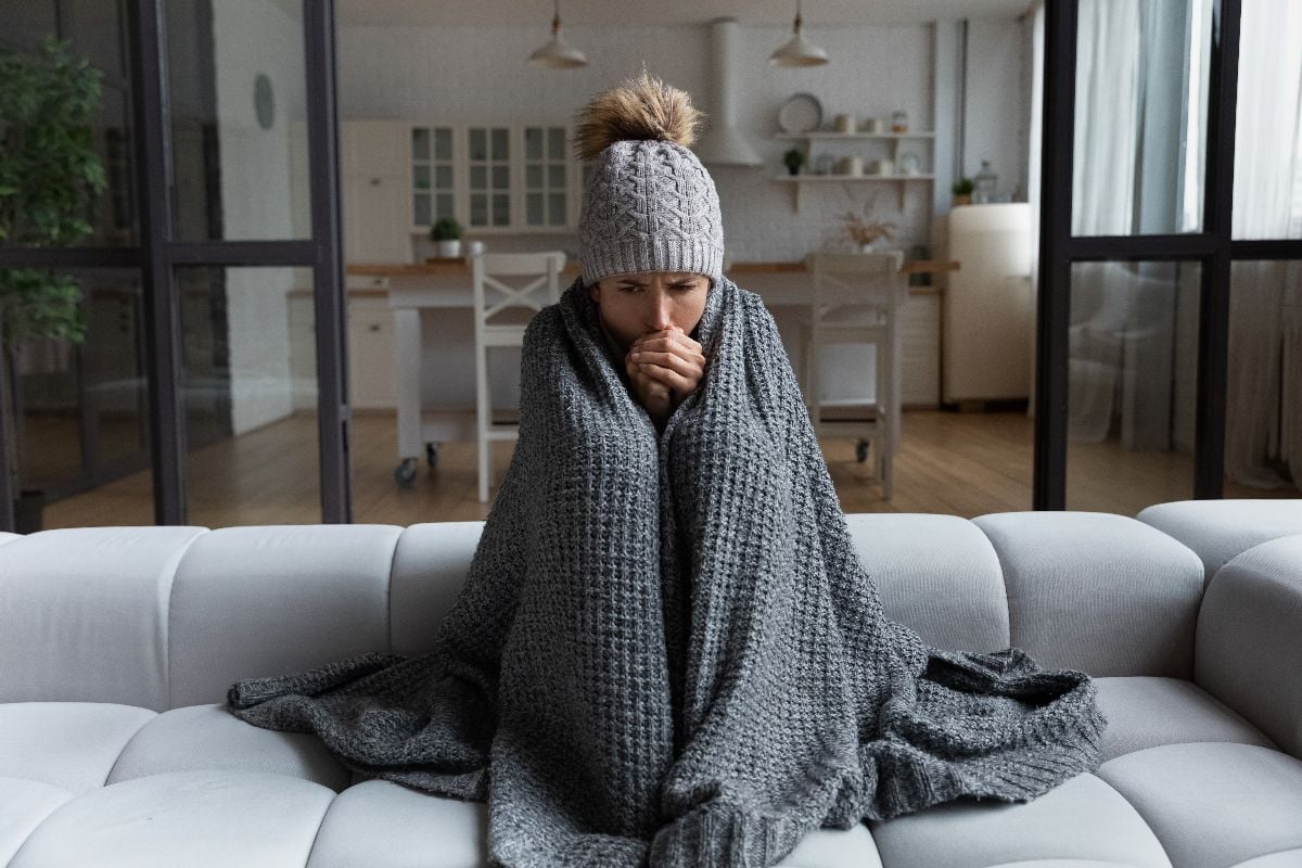 Woman covered in blanket, sitting on a couch.