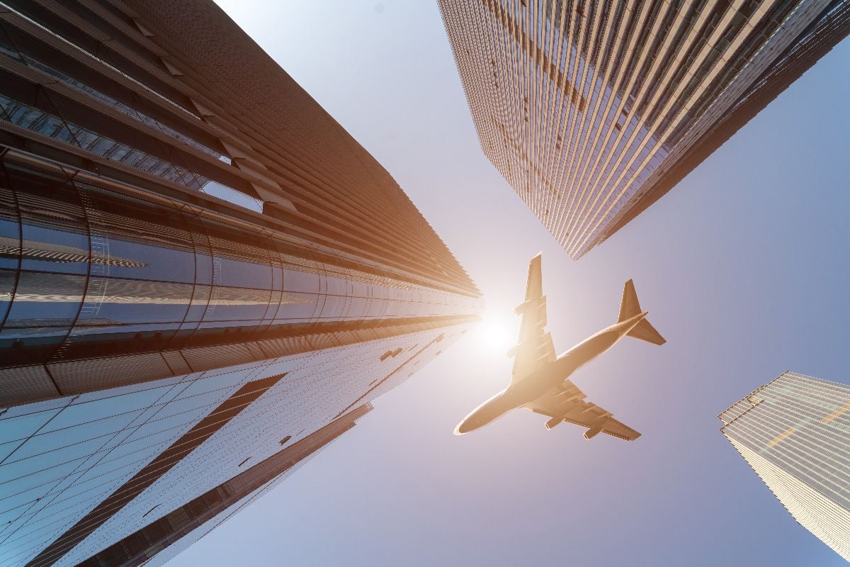 Low angle view of plane fly over modern office buildings.