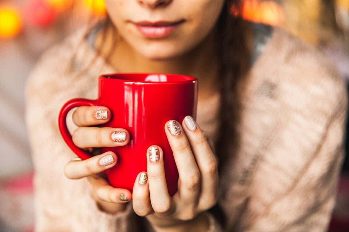 Woman's manicured hands holding a red cup of coffee. 
