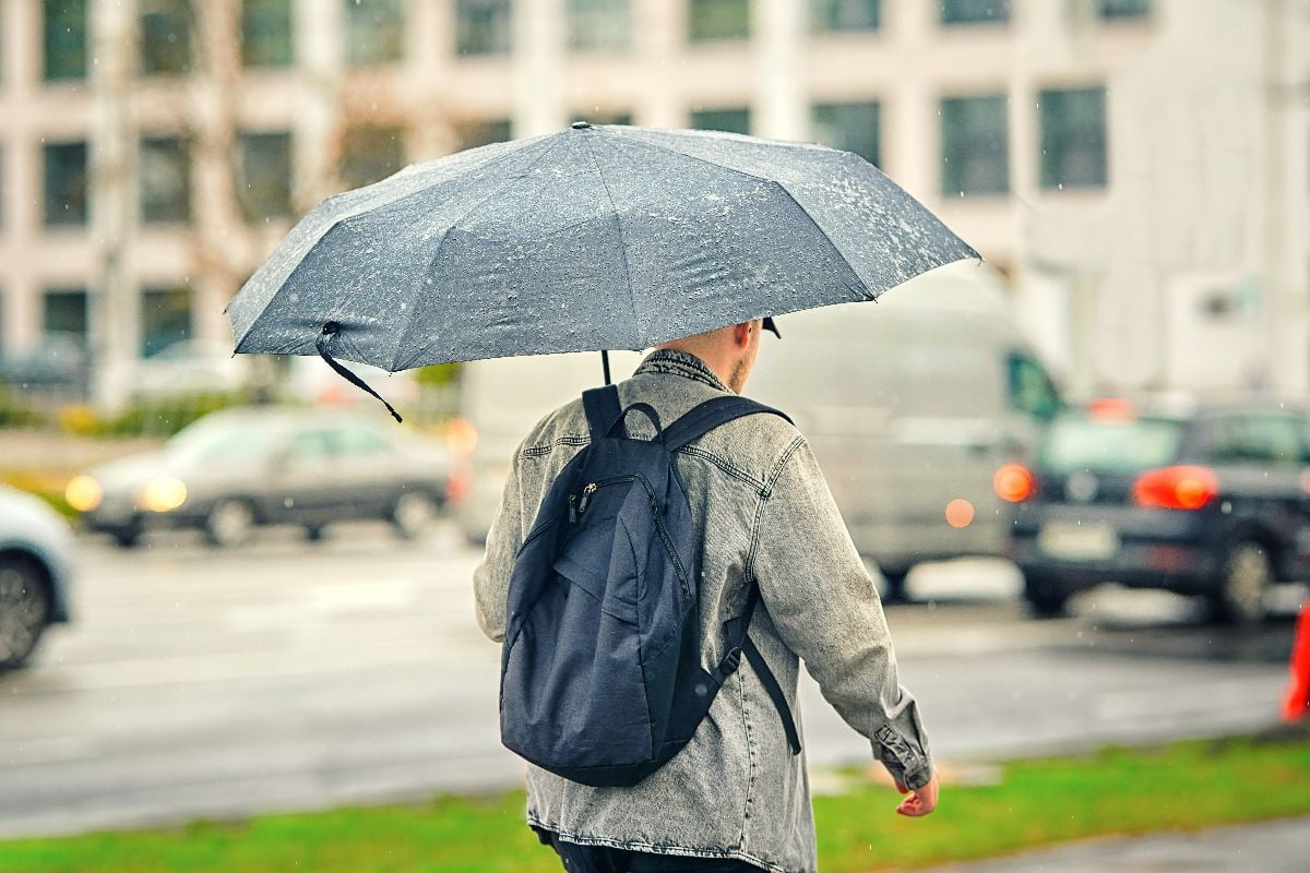 Man walking under black umbrella in heavy rain.