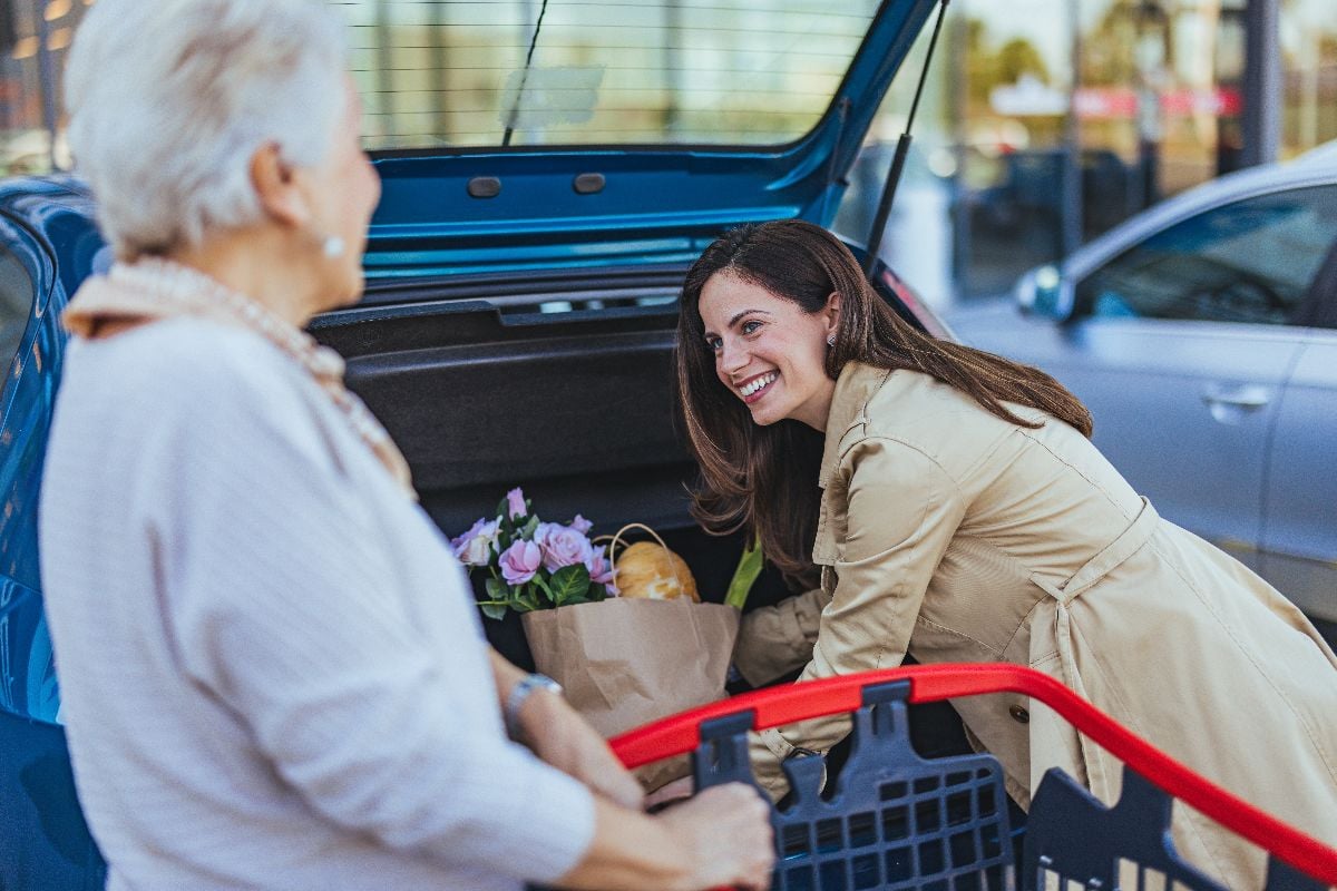 A young woman assists an elderly lady in loading groceries into a car the car.