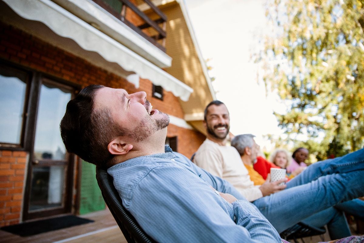 Group of happy neighbors laughing and enjoying while sitting together on a house porch.