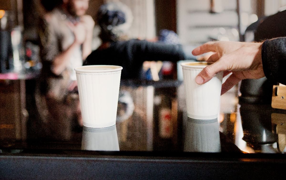A male hand grabs a take away coffee from a counter in a coffee shop.