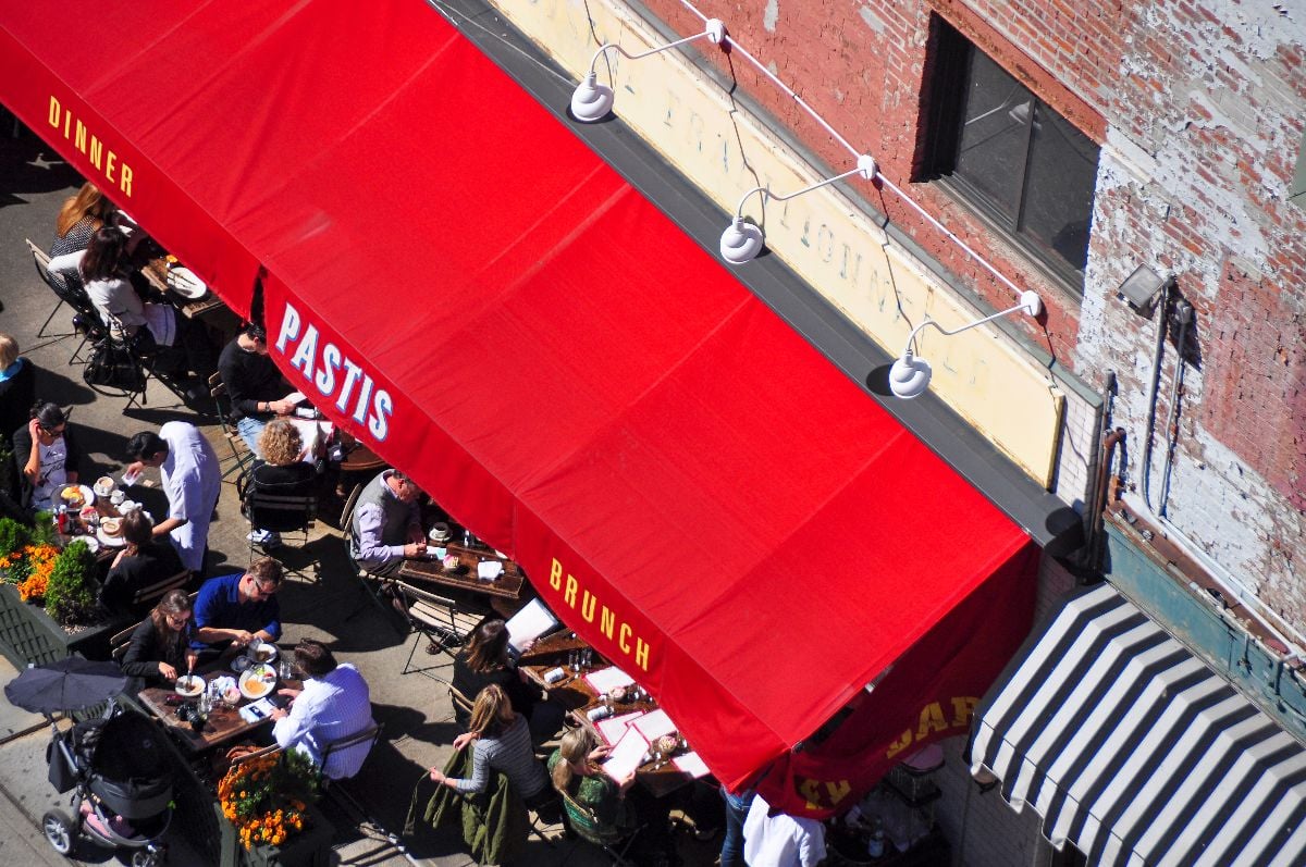 High angle view on the terrace with overhanging red awning of the French Bistro Pastis filled with people.