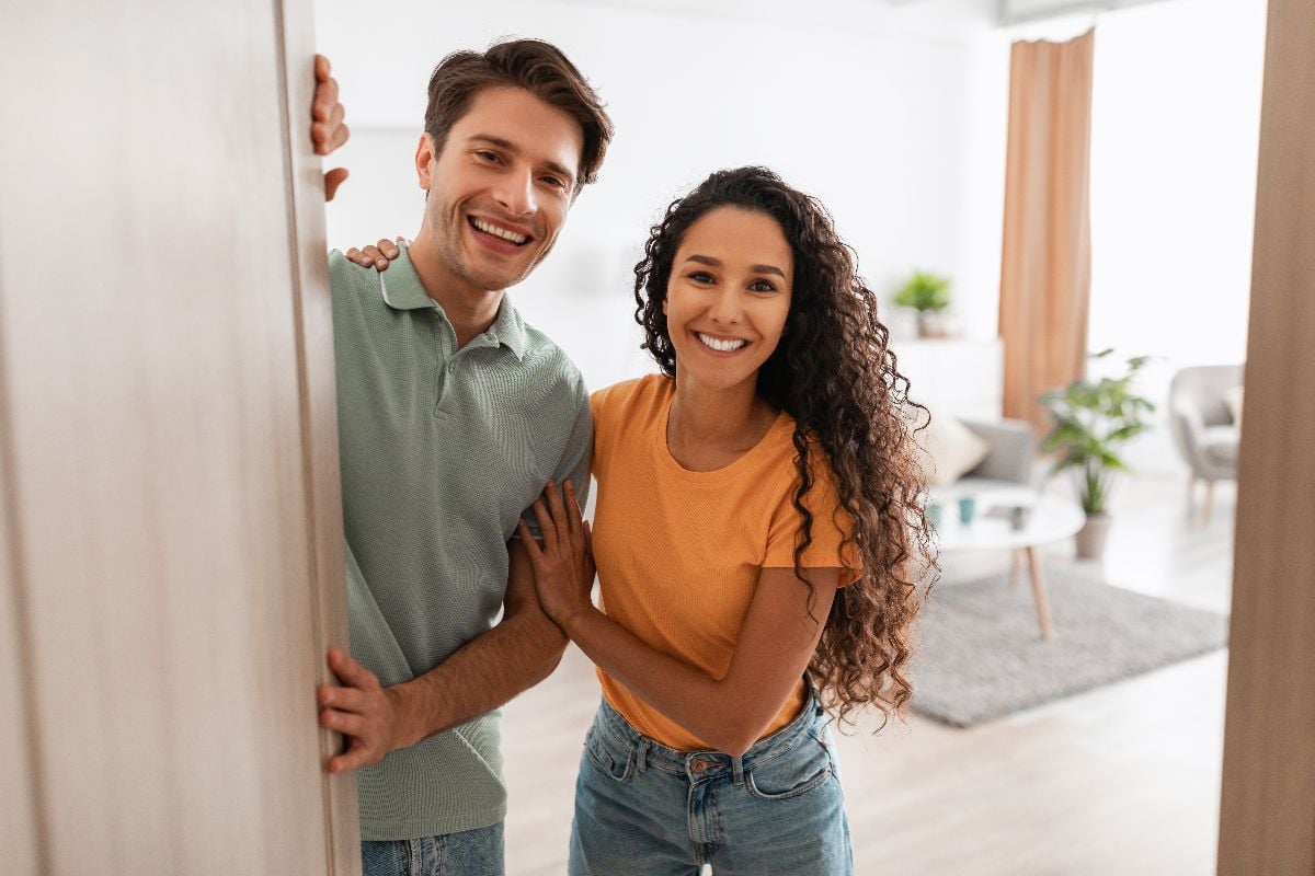 Portrait of excited couple inviting guest friends to enter their home.