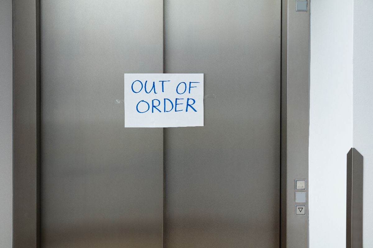 Written text "Out of Order" in white paper on a broken elevator.