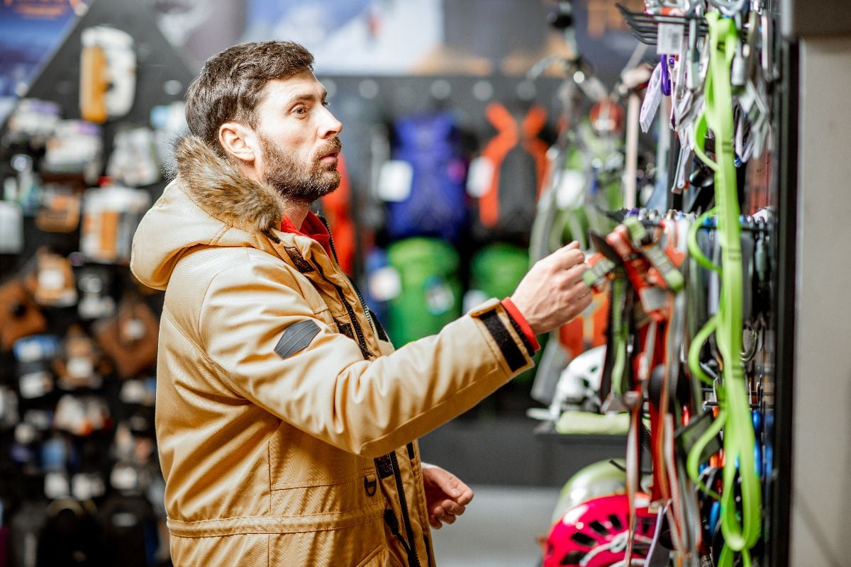 Man in winter jacket choosing mountaineer equipment in the sports shop.