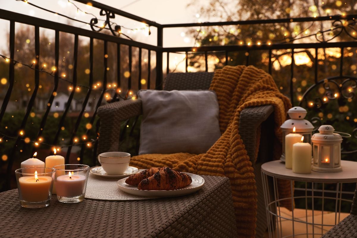 Beautiful view of garden furniture with pillow, soft blanket and burning candles at balcony.